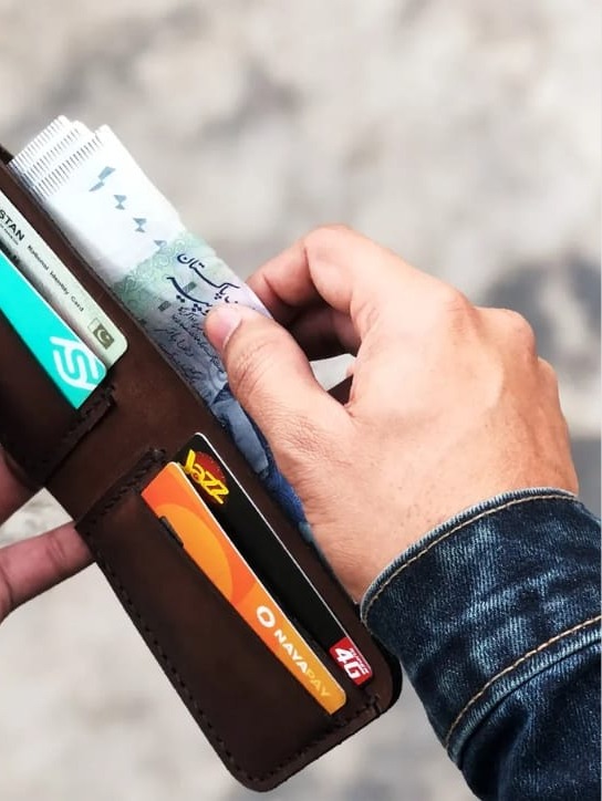 The Drifter Travel Wallet in espresso brown leather, closed, held in hand