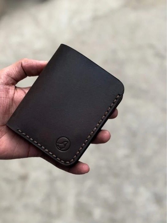 The Rancher Bifold Wallet in espresso brown leather, closed, held in hand